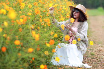 cute and beautiful girl with hat standing in nature outdoors among cosmos flowers field (rest time on vacation concept)