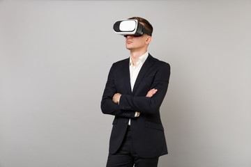 Young business man in classic black suit, shirt looking up in headset, holding hands crossed isolated on grey wall background in studio. Achievement career wealth business concept. Mock up copy space.