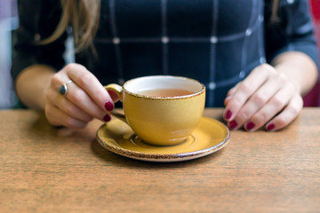 Girl holds yellow tea cup on the wooden table in cafe, close-up