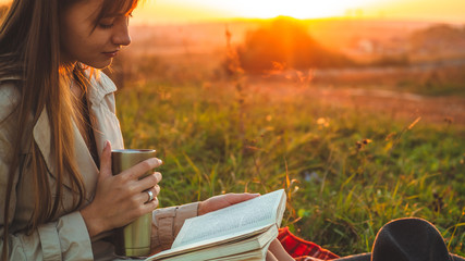 The concept of lifestyle outdoor recreation in autumn. Girl with hat read books on plaid with a...