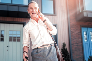 Laughing man. Stylish handsome man with tattoo on hand feeling very cheerful laughing while speaking by phone