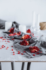 Pieces of red ripe pomegranate on grey towel on table with candles