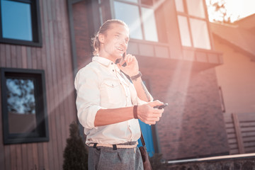Fototapeta premium Cheerful man. Handsome businessman feeling cheerful while calling his wife on way to work and opening his car