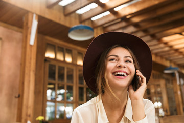 Close up of a laughing girl in hat sitting at the cafe