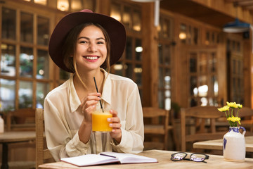 Smiling girl in hat sitting at the cafe table indoors