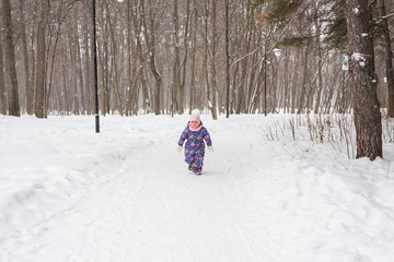 Winter, childhood and nature concept - baby girl walking in the winter outdoors