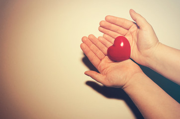 Hands holding a red heart on a solid white background