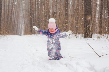Childhood and people concept - baby girl walking in the winter outdoors and throwing the snow up