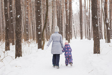 Fototapeta na wymiar Winter, family and people concept - Mother is walking with her little daughter in snowy park, back view