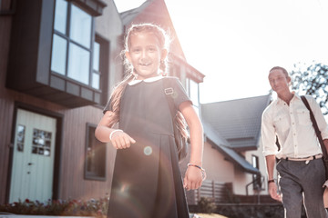 Blue uniform. Funny cheerful girl wearing dark blue school uniform smiling broadly while going to school