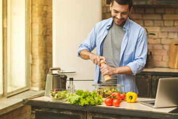 It's so delicious! Casual happy young man preparing salad at home in loft kitchen and smiling.