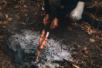 Obraz premium Different sausage on stick frying on campfire. Handmade grill. Outdoor recreation concept. 