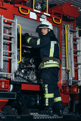 fireman in protective uniform and helmet looking at camera at fire station