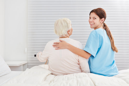 Fürsorgliche Pflegehilfe hilft Seniorin aus dem Bett