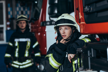 selective focus of female firefighter talking on portable radio set with colleague behind at fire...