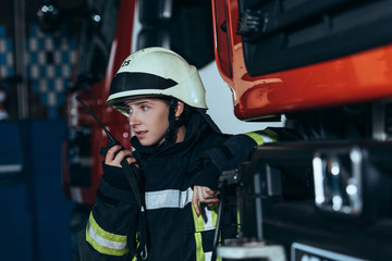 portrait of female firefighter in protective uniform talking into  portable radio set at fire...