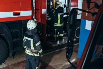 partial view of firefighters in fireproof uniform and helmets at fire station