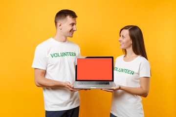 Colleagues couple in white t-shirt inscription volunteer hold laptop pc computer, blank empty...