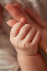 Close-up. Beautiful young mother holds the baby in her arms. Mom holds baby hands. Love. Motherhood. Happiness. House. Cozy.