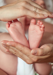 Close-up. Beautiful young mother holds the baby in her arms. Mom holds the baby's legs in her hands for 3 months. Love. Motherhood. Happiness. House. Cozy.