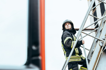 female firefighter in protective uniform and helmet standing on ladder on street © LIGHTFIELD STUDIOS