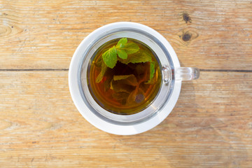 Black tea with mint in glass on the white plate and wooden table, top view with copy space