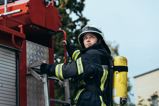 female firefighter with fire extinguisher on back standing on fire truck on street