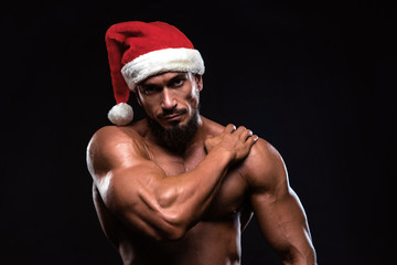 Fototapeta na wymiar Muscular man in christmas hat is showing bicep putting is hand on the shoulder