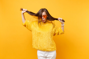 Fototapeta na wymiar Pretty young woman in fur sweater, heart orange glasses fool around, holding her hair like ponytails isolated on bright yellow background. People sincere emotions, lifestyle concept. Advertising area.