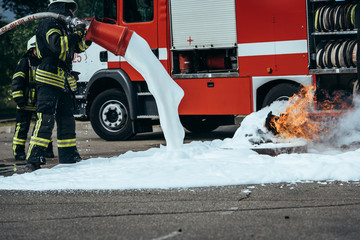 partial view of firefighter extinguishing fire with foam on street