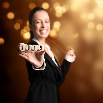 junge lachende Geschäftsfrau vor Silvesterhintergrund hält  Würfel mit der Aufschrift 2019 in die Kamera