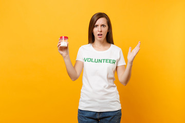 Portrait of woman in white t-shirt written inscription green title volunteer holding bottle with pills drug isolated on yellow background. Voluntary free assistance help, charity grace health concept.