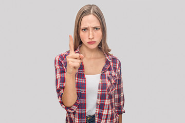 Sad and unhappy young woman points up. She looks on camera with sad face. Beautiful model is upset. Isolated on grey background.