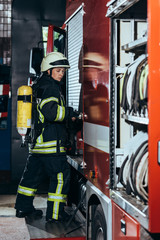 side view of female firefighter with fire extinguisher on back closing truck at fire station