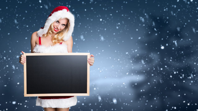Weihnachtsfrau mit leerer Kreidetafel für eigene Nachricht vor Winterlandschaft 