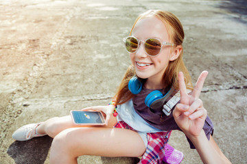 Cool teenager. Joyful young female wearing sunglasses and checking weather forecast on her gadget