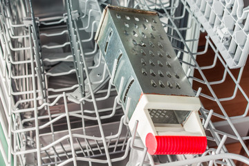 Iron grater with a red handle lies in the dishwasher