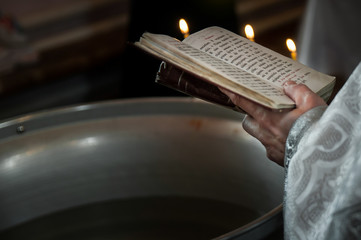 Priest praying in the church holding holly bible and cross with candles