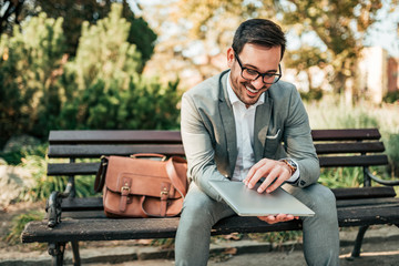 Happy elegant men sitting on a bench with a laptop.