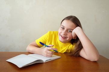 Happy girl writing in notebook placed on wooden desktop with background of grunge grey wall, Children, education and learning concept