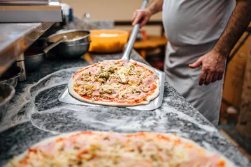  Chef-kok die rauwe pizza op metalen schop neemt om in de oven te bakken. © bnenin