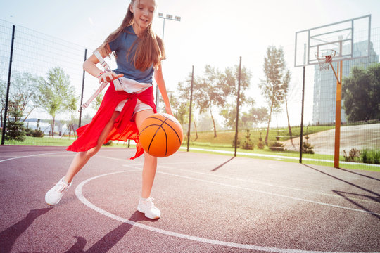 Beat it. Charming sporty teenager keeping smile on face while looking at orange ball