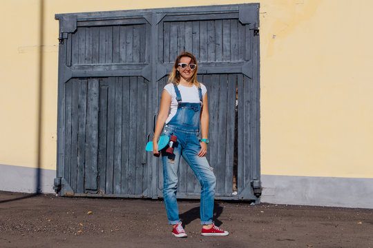 Portrait of a smiling woman standing with her skateboard next to the old wooden wall.