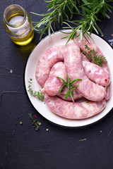 Fresh homemade raw sausages on plate  on black textured background.