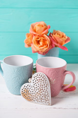 Two cups and hearts and  fresh orange roses  against  turquoise  wall.