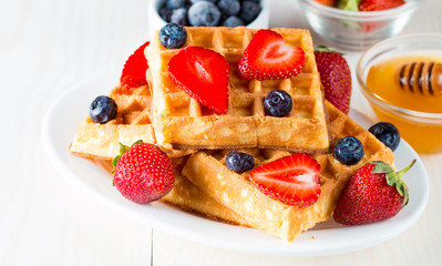 Photo of fresh homemade food made of berry Belgian waffles with honey, chocolate, strawberry, blueberry, maple syrup and cream. Healthy dessert breakfast concept with juice. 