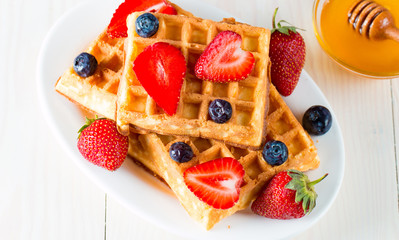 Photo of fresh homemade food made of berry Belgian waffles with honey, chocolate, strawberry, blueberry, maple syrup and cream. Healthy dessert breakfast concept with juice. 