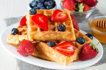 Photo of fresh homemade food made of berry Belgian waffles with honey, chocolate, strawberry, blueberry, maple syrup and cream. Healthy dessert breakfast concept with juice. 