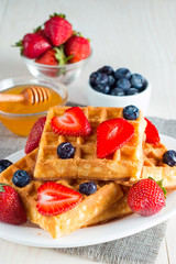 Photo of fresh homemade food made of berry Belgian waffles with honey, chocolate, strawberry, blueberry, maple syrup and cream. Healthy dessert breakfast concept with juice. 