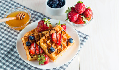 Photo of fresh homemade food made of berry Belgian waffles with honey, chocolate, strawberry, blueberry, maple syrup and cream. Healthy dessert breakfast concept with juice. 